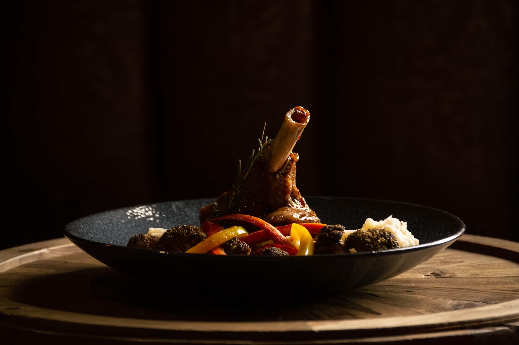 黒い皿に盛られた骨付き肉と色鮮やかな付け合わせ